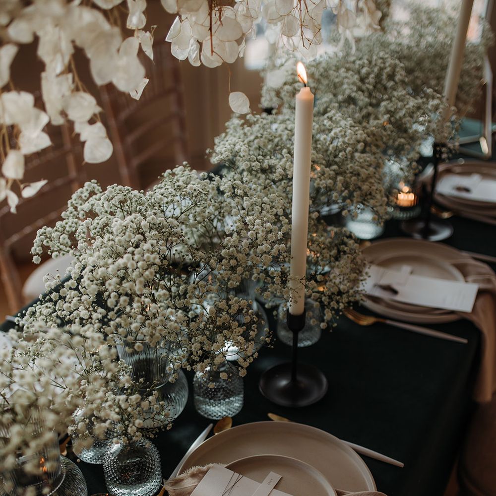 elegant wedding table decor with black table cloth, beige tableware, linens and taper candles and gypsophila centrepiece flowers 