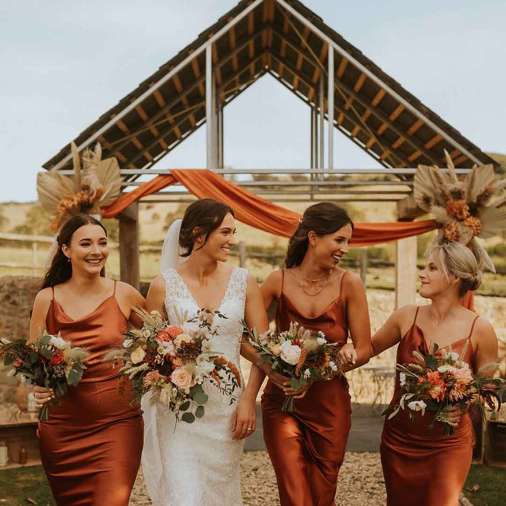 Bridal party in burnt orange bridesmaid dresses with orange floral bouquets 