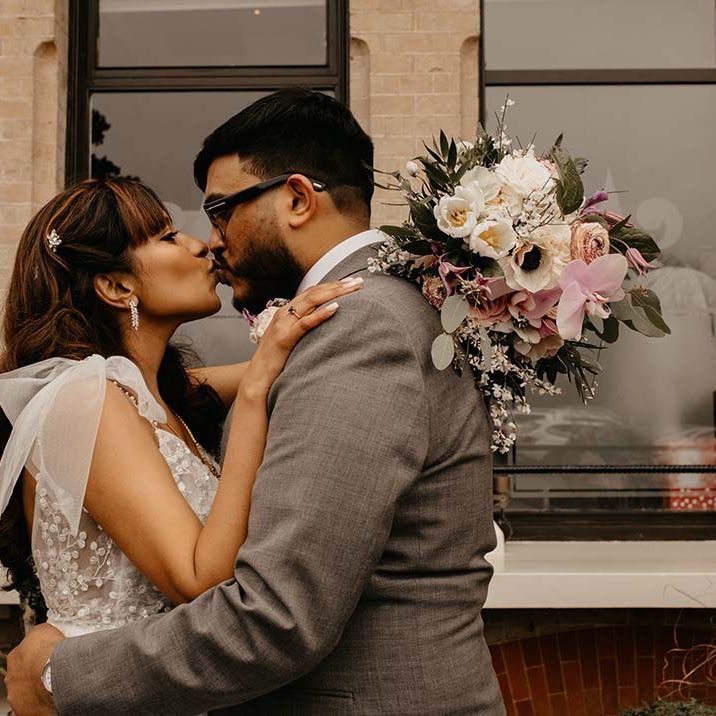 Bride in white wedding dress with embellishments and mixed flower bouquet embracing groom in grey suit