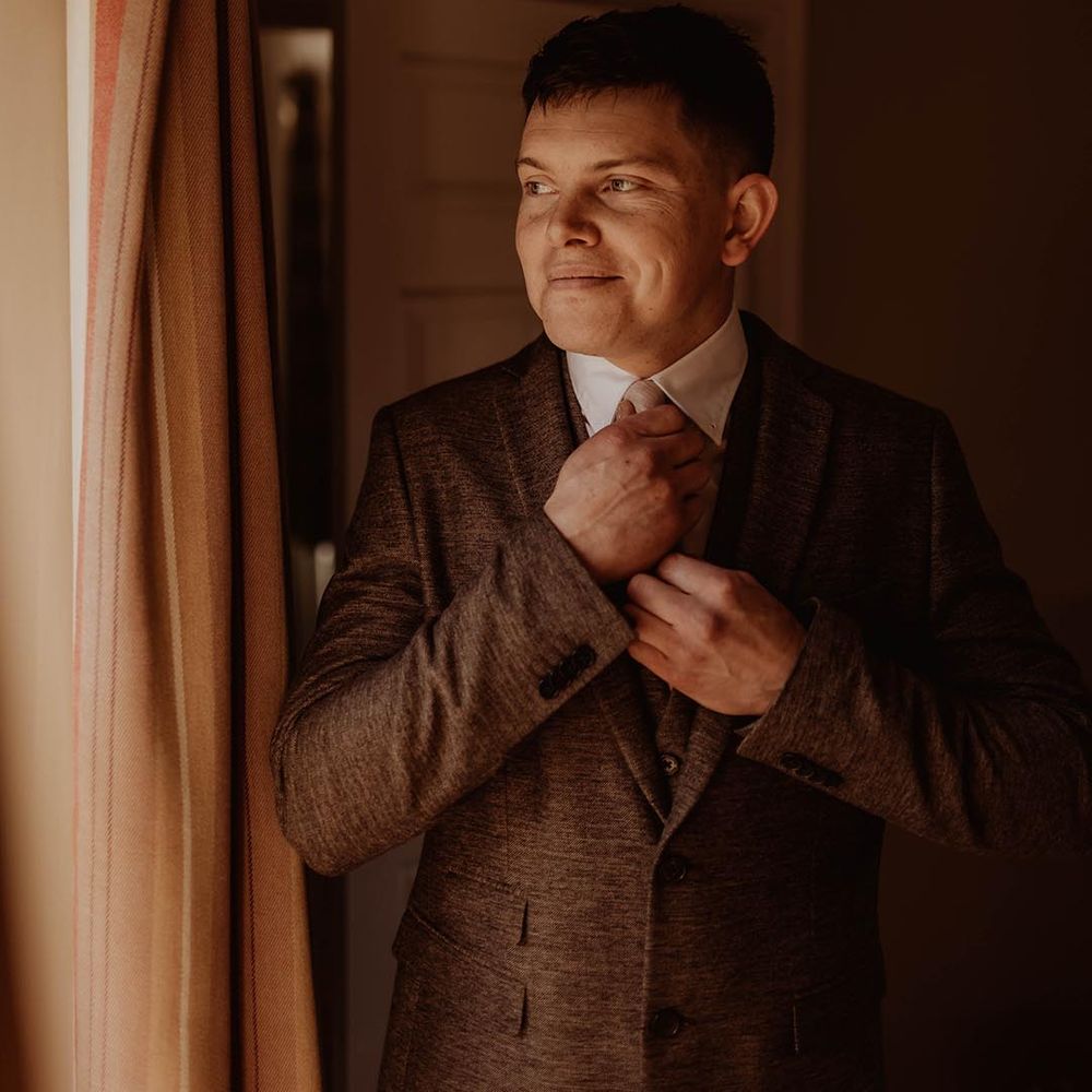 Groom fixes his tie as he gets ready for his wedding day at Eden Barn