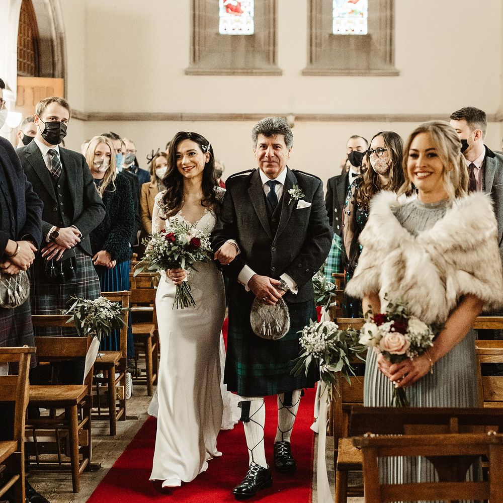 Bride walks down the aisle holding red and white floral bouquet for winter wedding in Scotland 