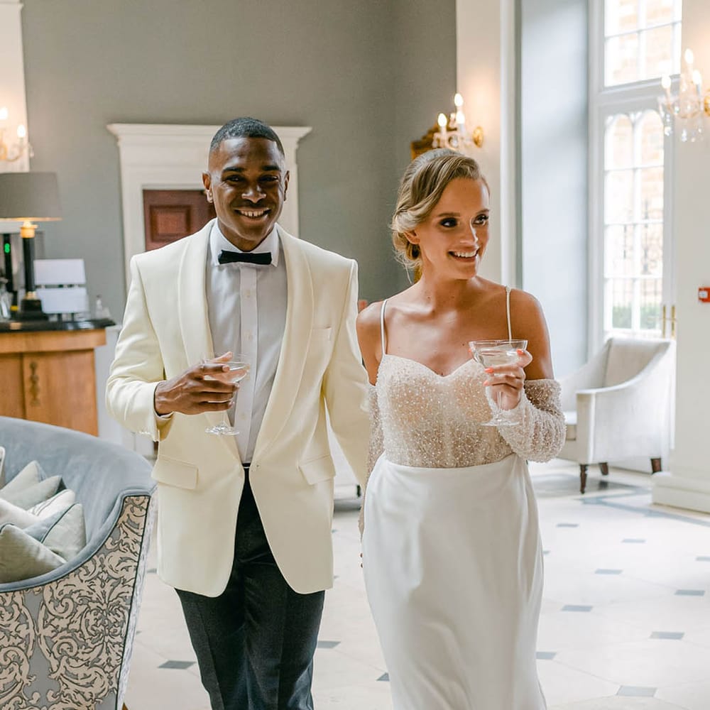 Bride in beaded off the shoulder second wedding dress with the groom wearing a white suit jacket and black trousers for the evening 