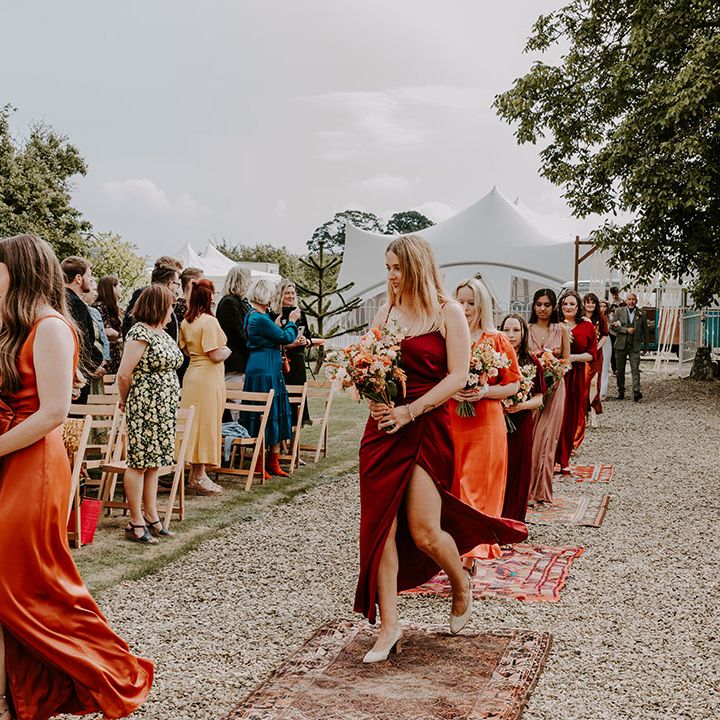 Bridesmads in Autumnal colour bridesmaid dresses walk down the aisle during outdoor wedding ceremony 