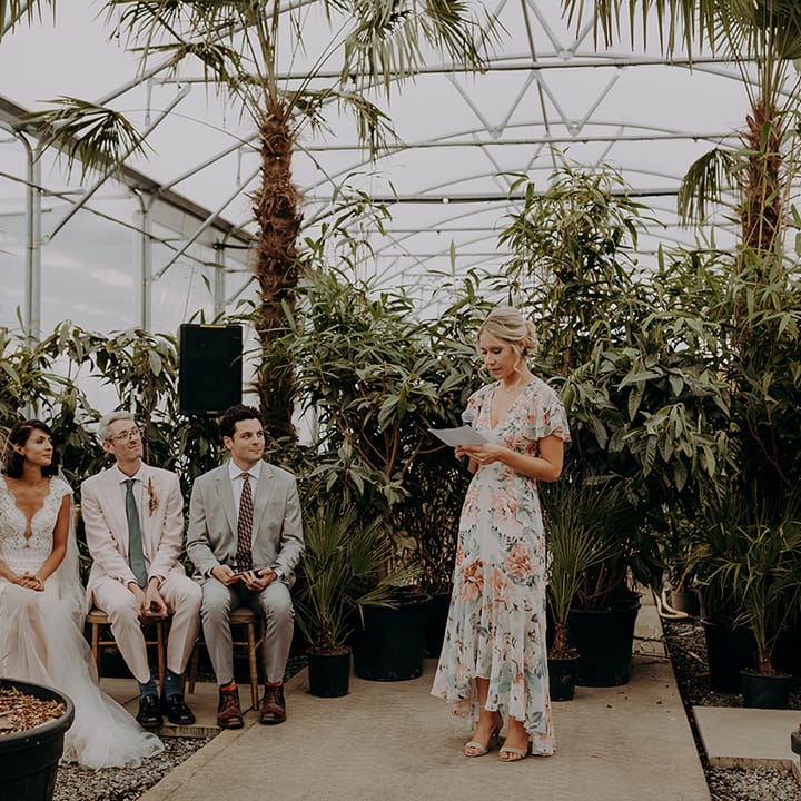 Bridesmaid in floral dress does reading at front of ceremony with greenery in background
