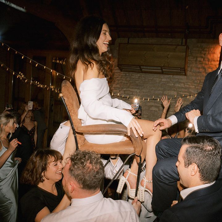 The bride and groom sit on chairs and are lifted up by their wedding guests for a Jewish wedding tradition  