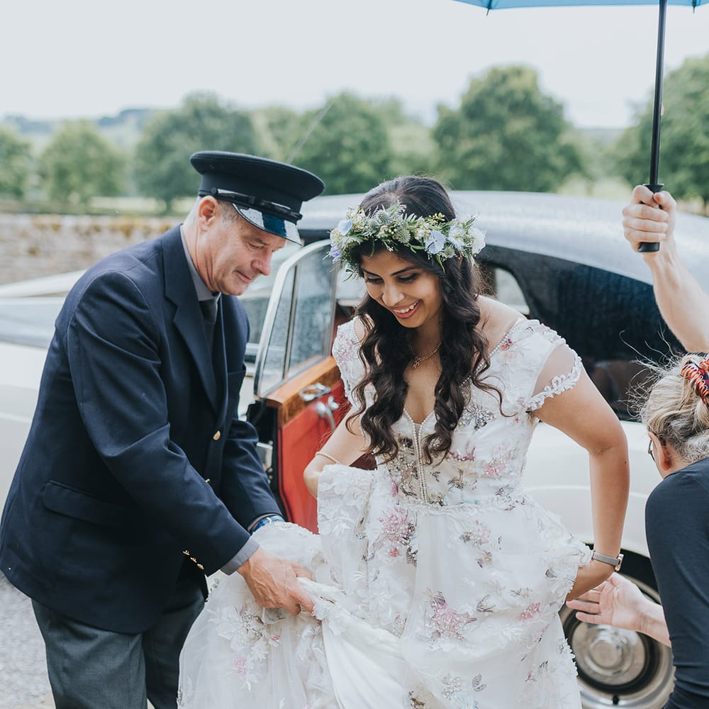 Bride in a floral Savin London Amelia Dress getting our of her classic wedding car