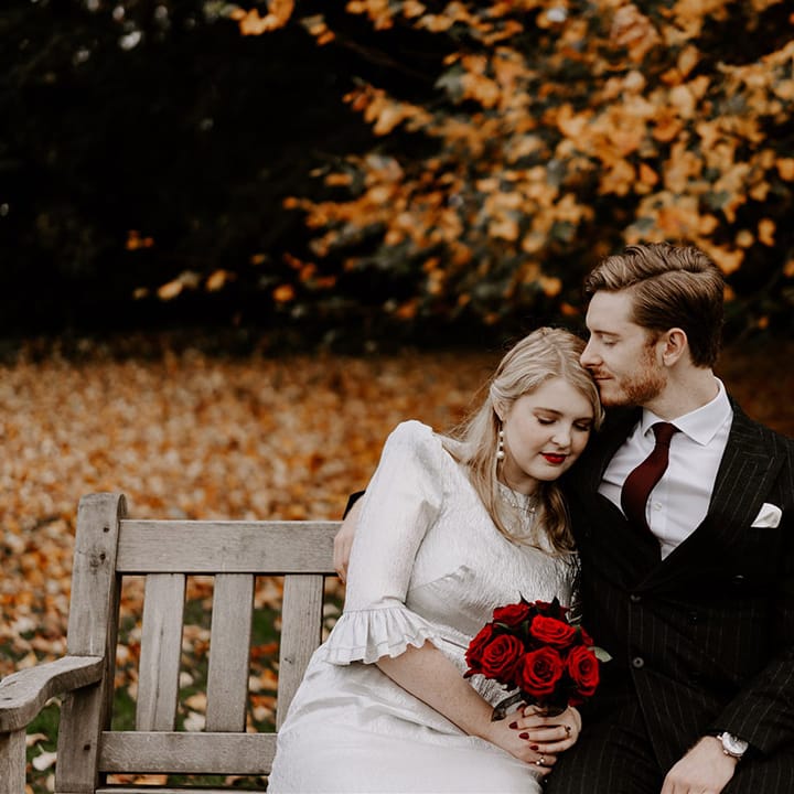 Bride in sparkly wedding dress with shoulder pads and ruffle sleeves holding red rose bouquet with the groom in pinstriped suit 
