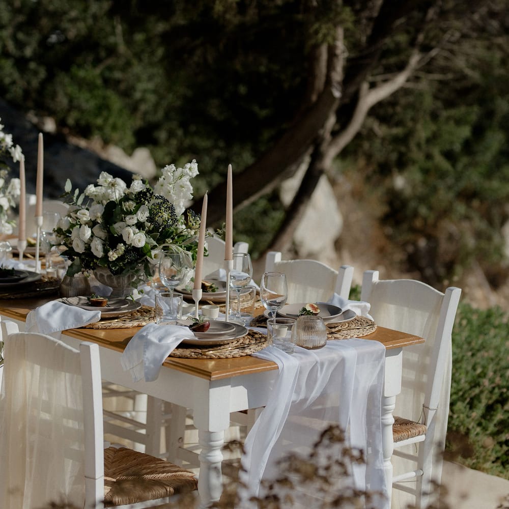 Greek wedding tablescape featuring blush tapered candles, figs, ribbed jars, wine glasses and floral decor that includes white berries, italian ranunculus and eucalyptus