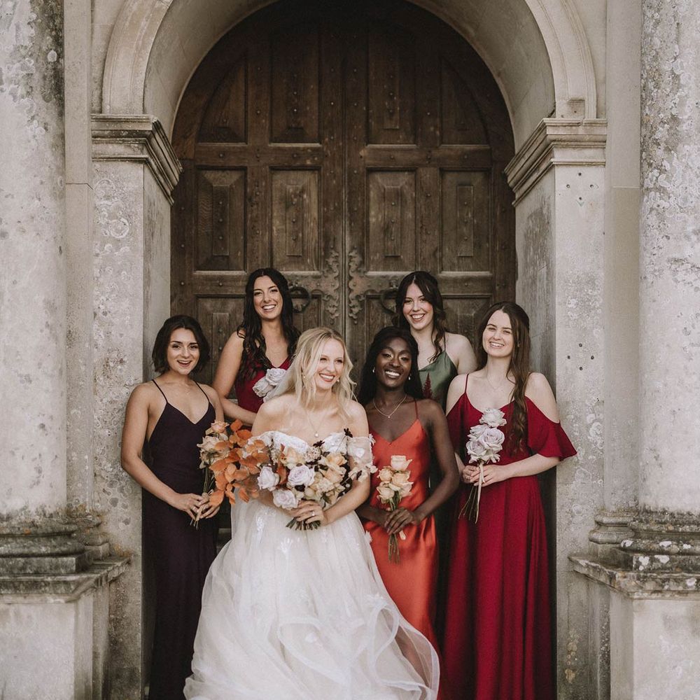 Bride in off shoulder princess wedding dress standing with bridesmaids in satin mismatched bridesmaid dresses 