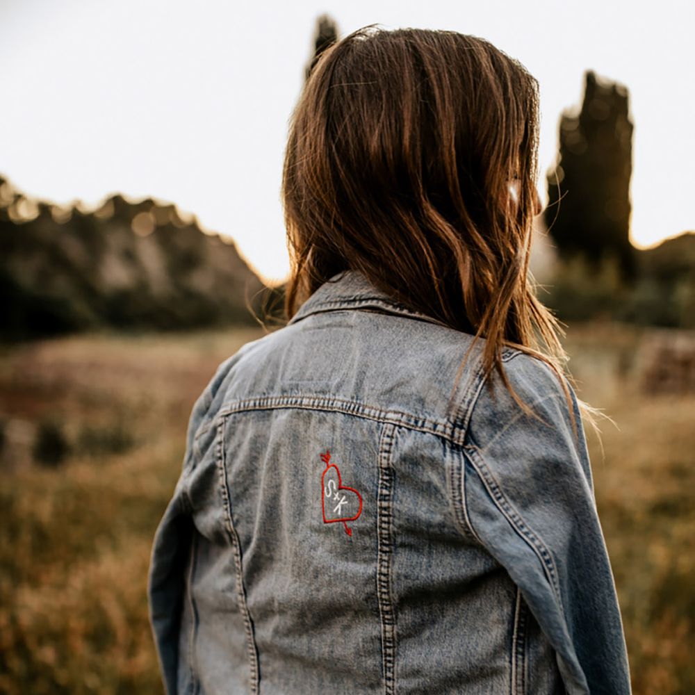 Bride in a classic blue denim jacket with a small embroidered arrow going through a heart with the bride and groom's initials 