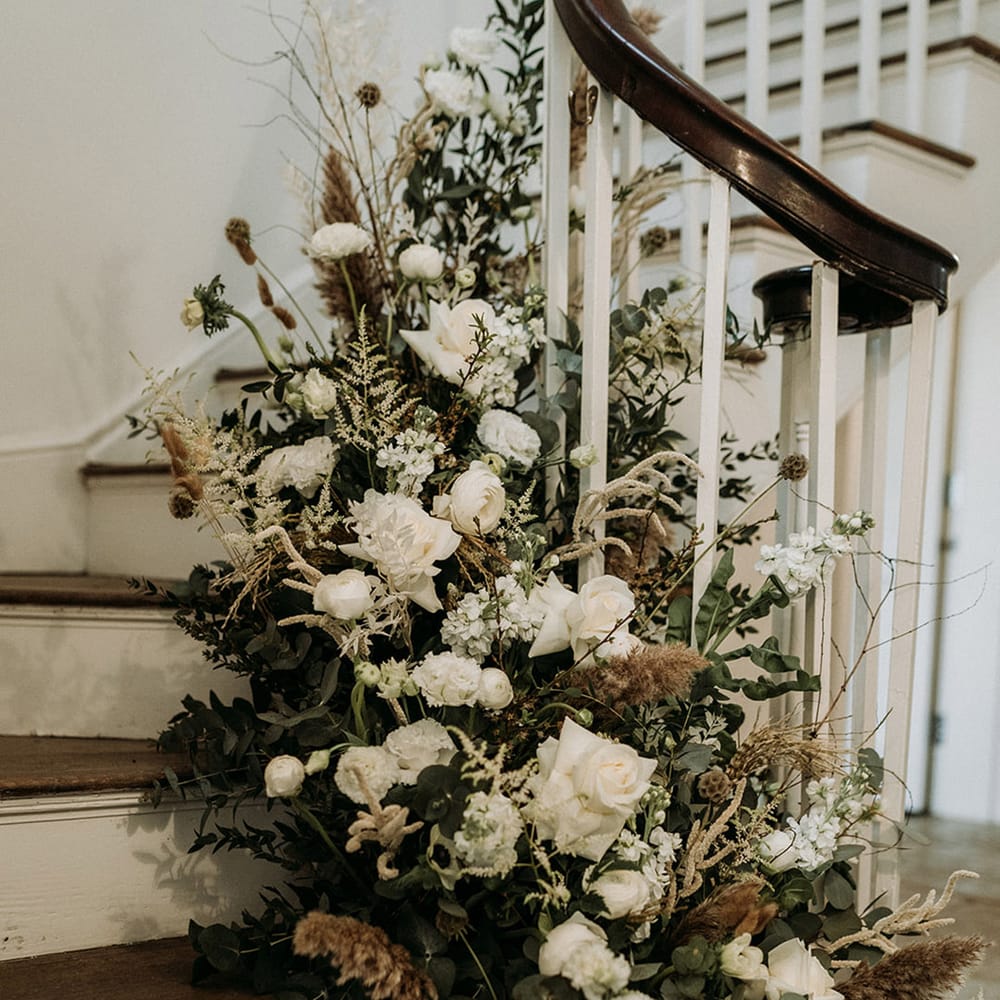 All white wedding flowers decorating the staircase at Aswarby Rectory with dried grass for natural style wedding 