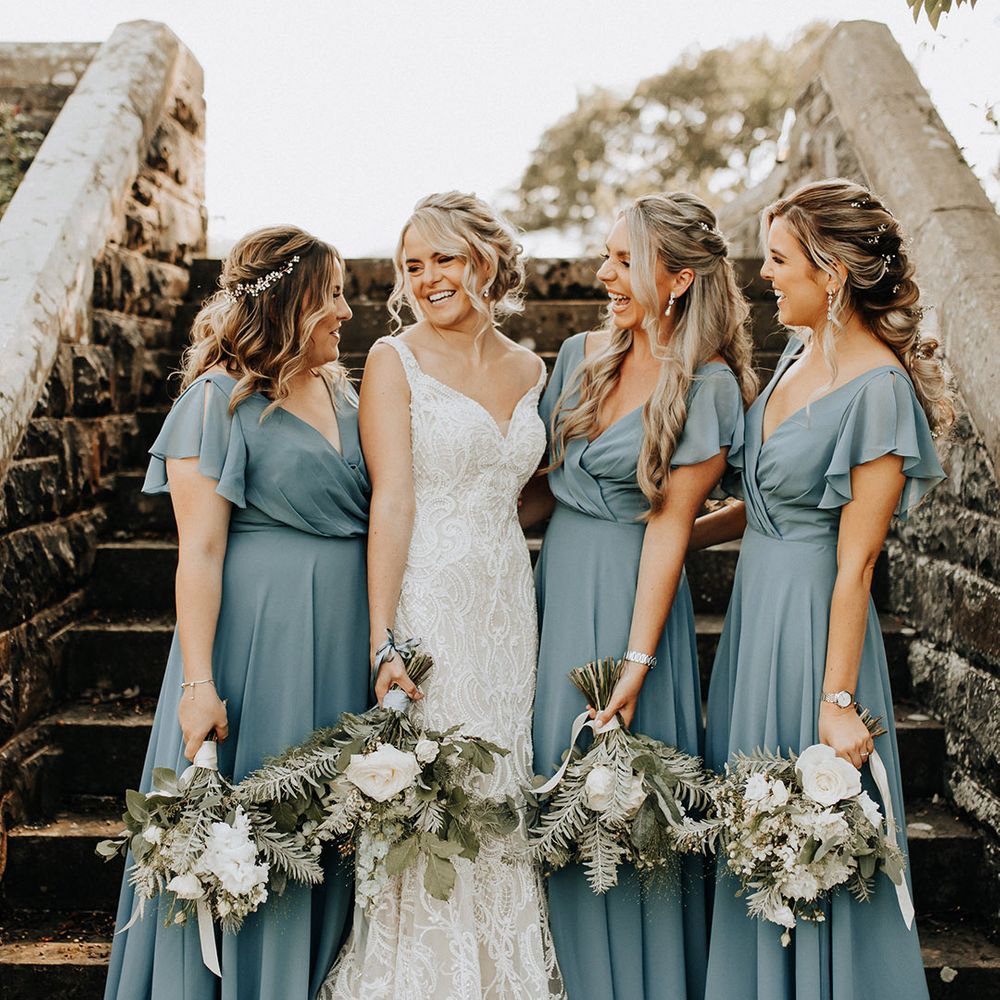 Country house wedding with the bridal party wearing ruffle sleeve blue bridesmaid dresses with white flower bouquets 