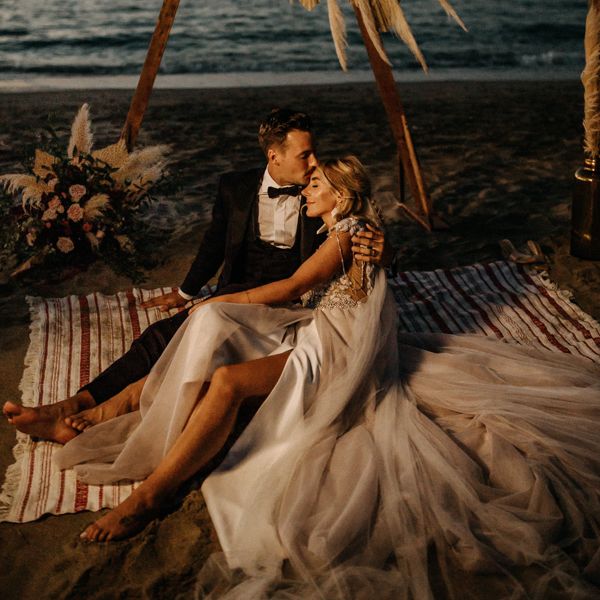 Bride and groom sit on the sand at night