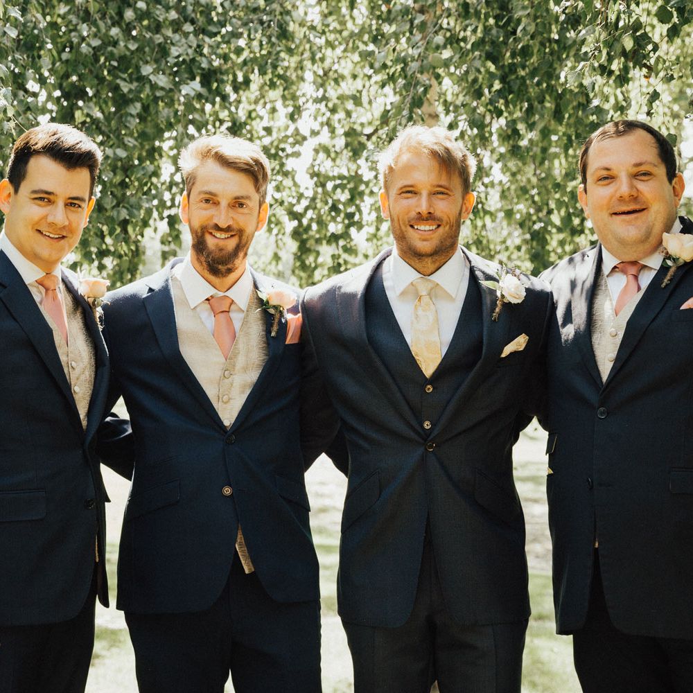 Smiling groomsmen in navy suits with pink and gold silk ties