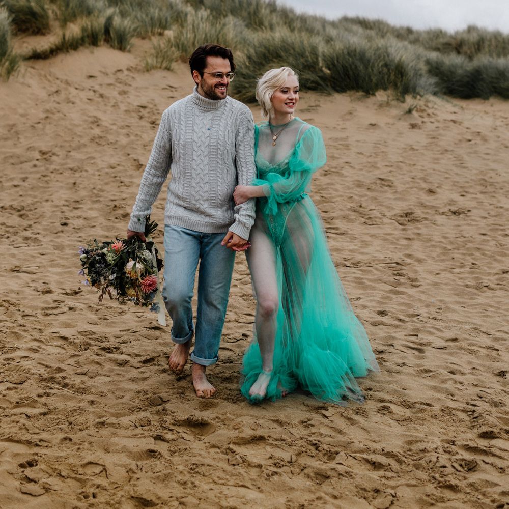 Stylish bride and groom walking barefoot in the sand at their intimate beach elopement 
