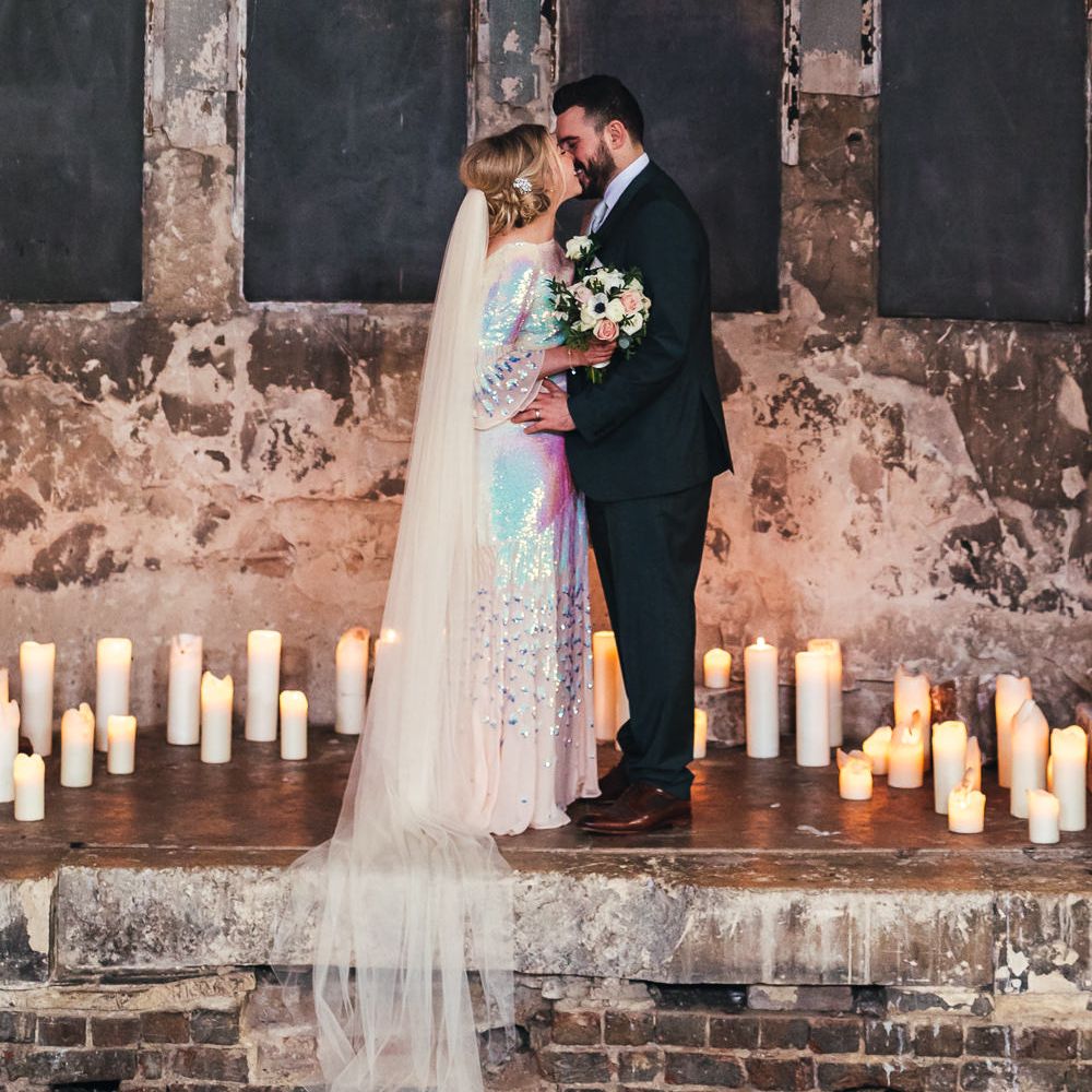 Bride & groom kiss at The Asylum surrounded by candles and industrial brick wall