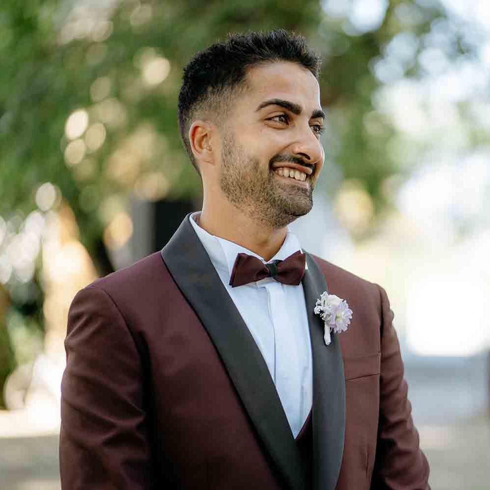 Groom in maroon suit with bowtie as he wait for his bride