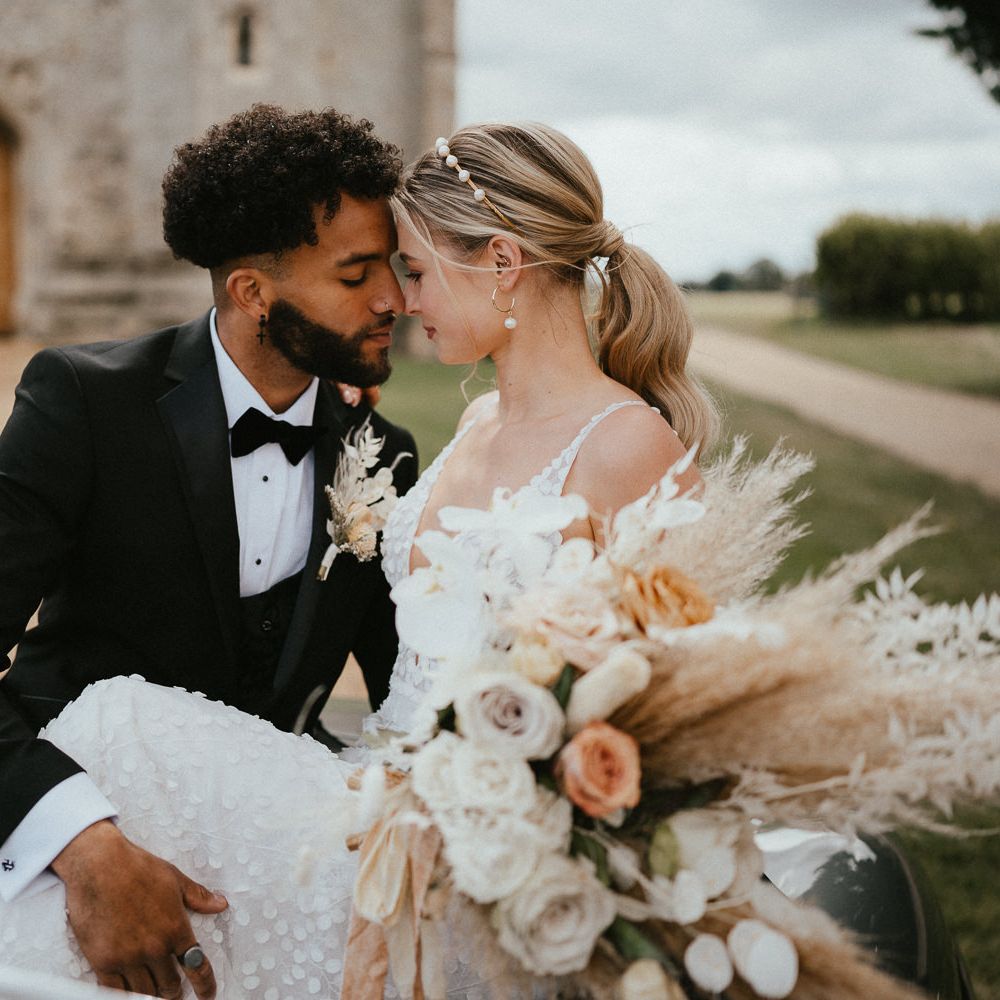 beaded groom in a three piece suit embracing his bride in a fitted wedding dress on the car bonnet 
