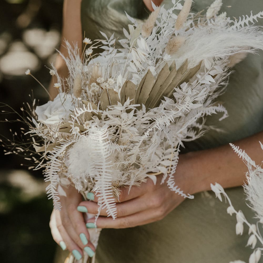 Bridesmaid in a sage green satin dress holding a dried flower bouquet with green nail polish