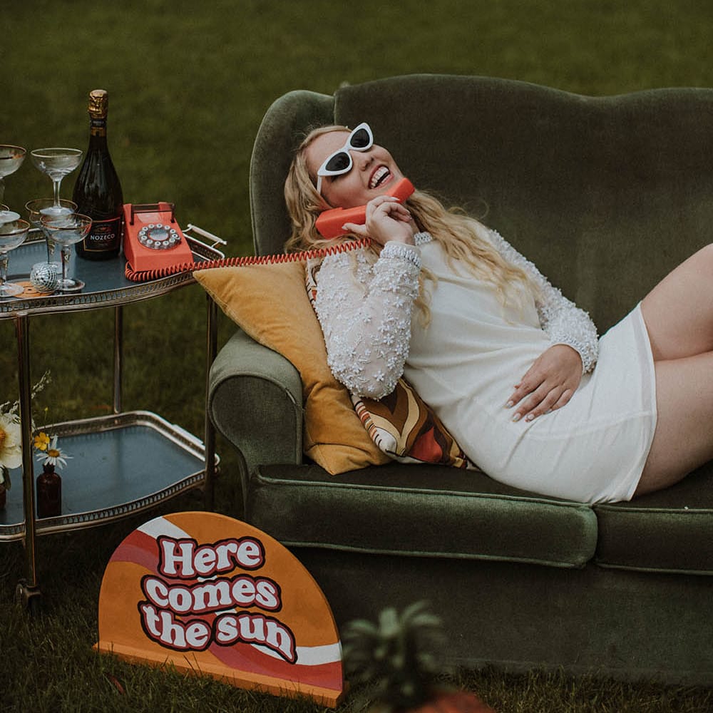Bride in a short wedding dress laying on a retro sofa answer a telephone with sunglasses on