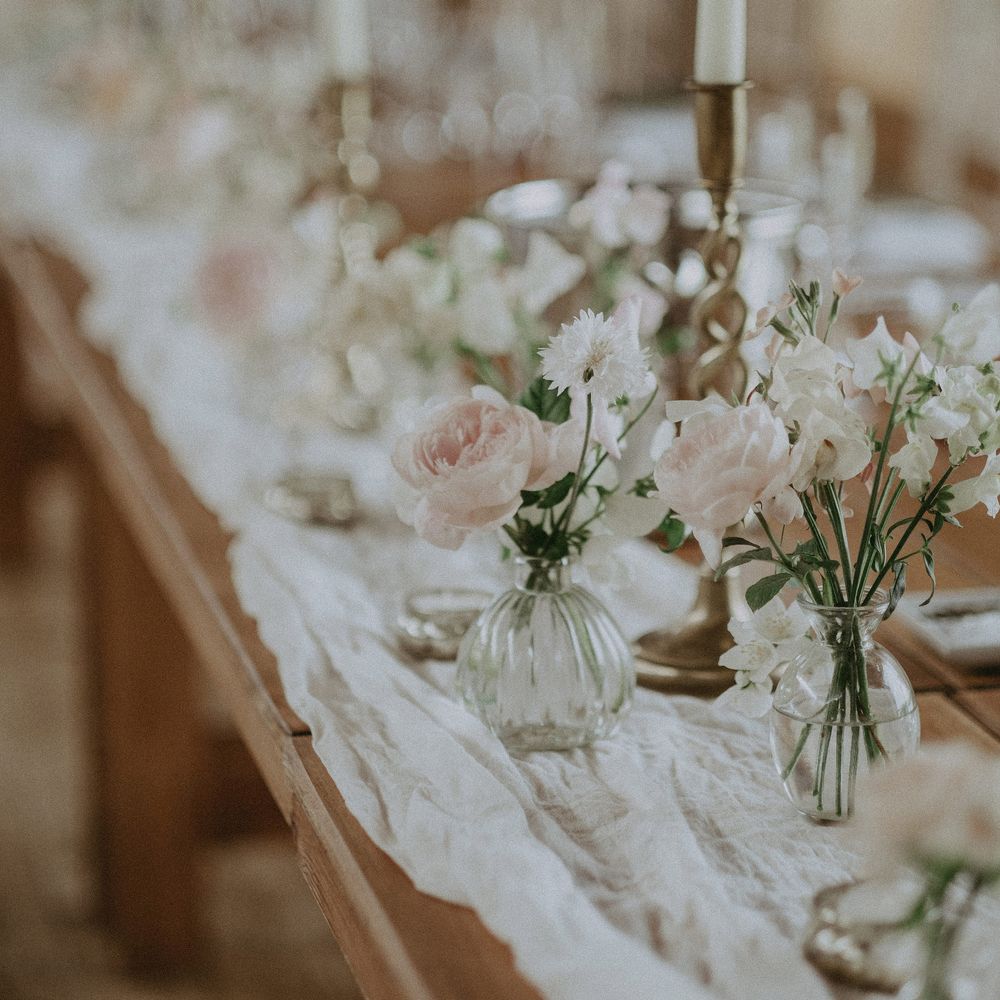Pastel pink florals sit within small vases with green foliage for elegant reception table decor