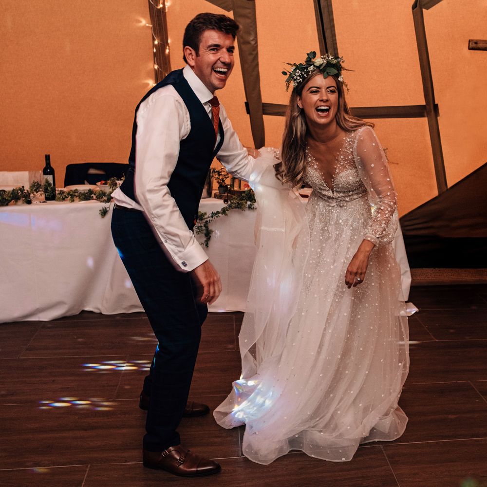 Bride in embroidered long sleeve wedding dress and flower crown dances with groom in waistcoat and red tie at tipi wedding reception