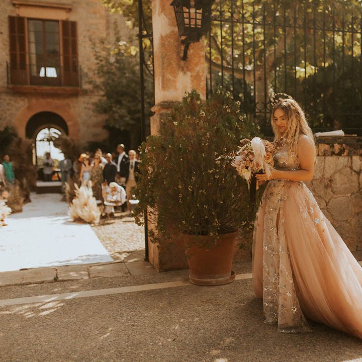 Bride walks to outdoor ceremony whilst holding bouquet 