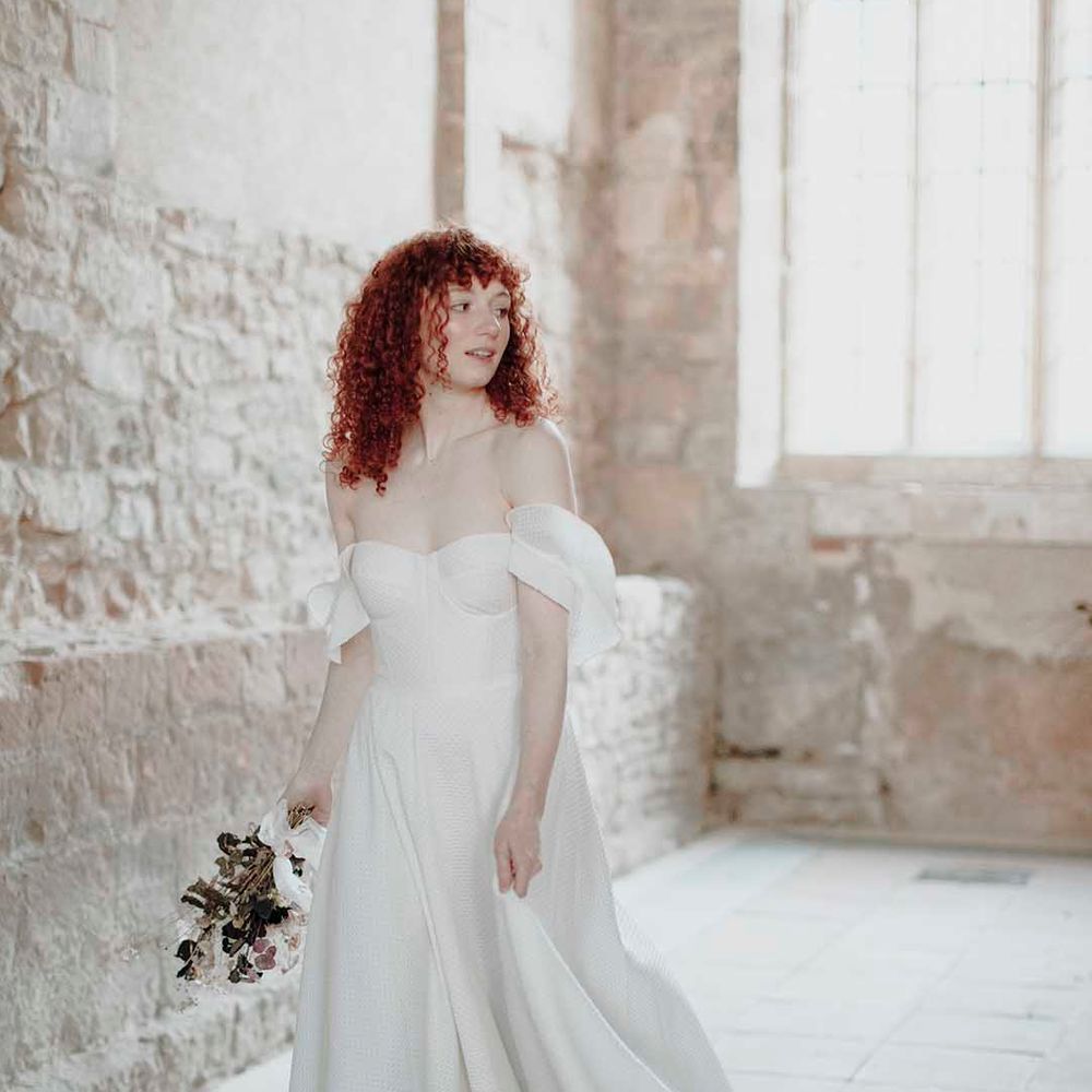 Bride with naturally curly red hair in a strapless wedding dress with Bardot sleeves and full skirt 