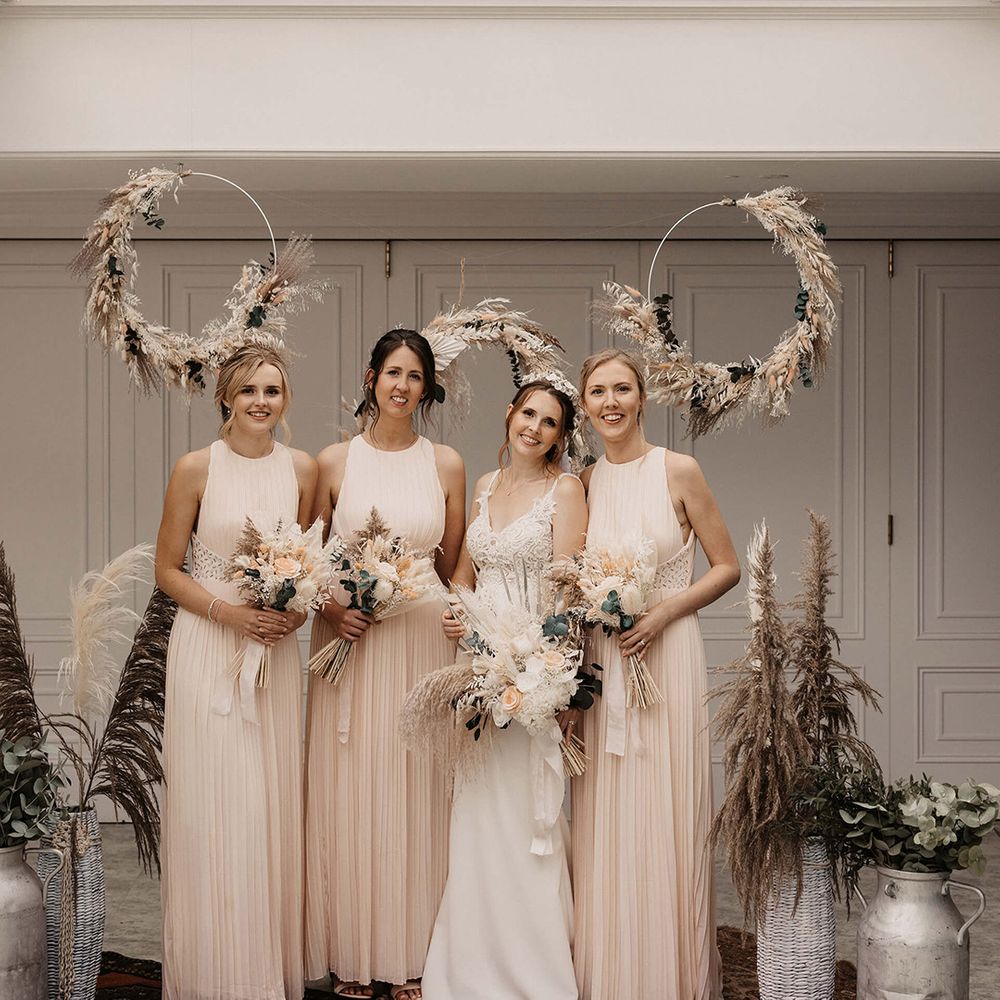 Bridesmaids stand with their bride in front of circular pampas grass installation 