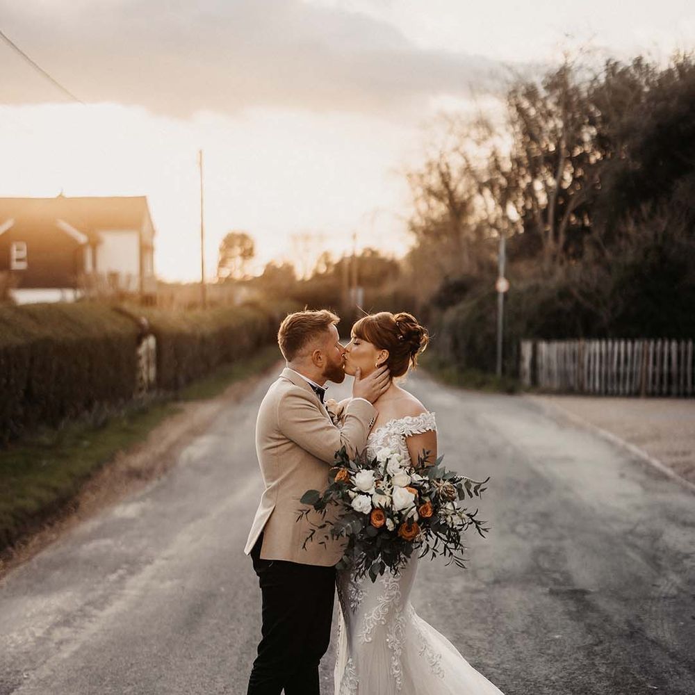 Bride and groom share a kiss for couple's portraits with white and orange wedding bouquet