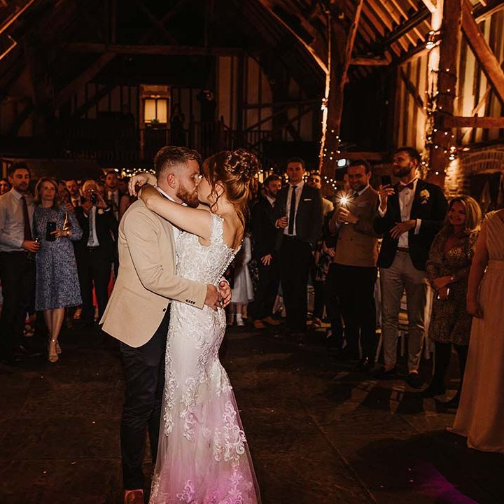 Bride and groom share their first dance in rustic Cooling Castle Barn wedding venue as the guests watch