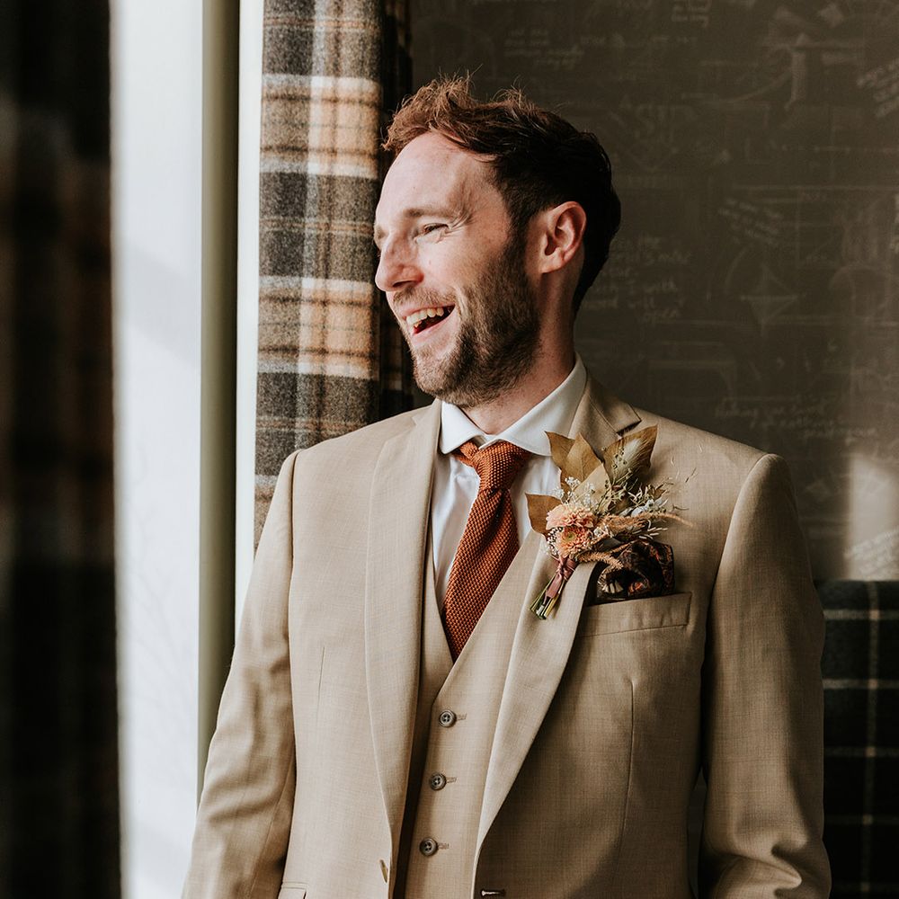 Groom in beige three piece suit with orange tie and dried flower boutonniere and patterned handkerchief 