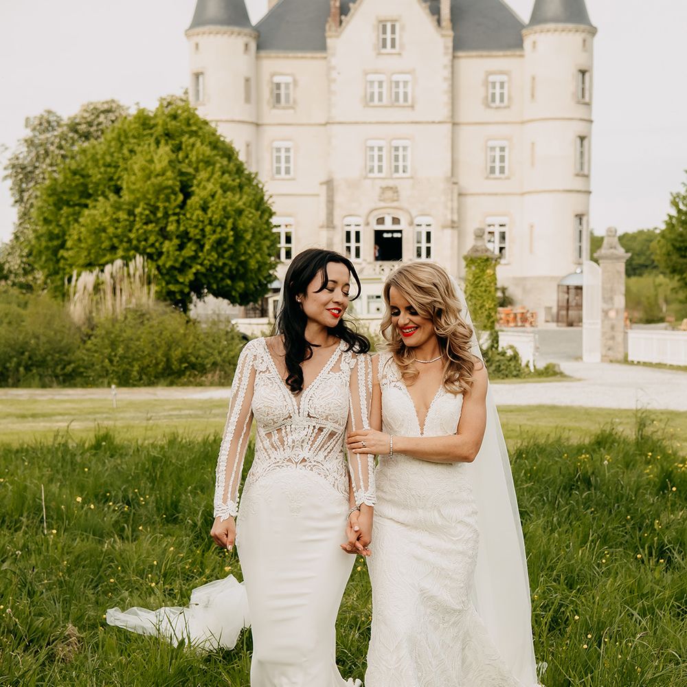 Bride in long sleeve illusion lace wedding dress and bride in v neck lace wedding dress walk holding hands together 