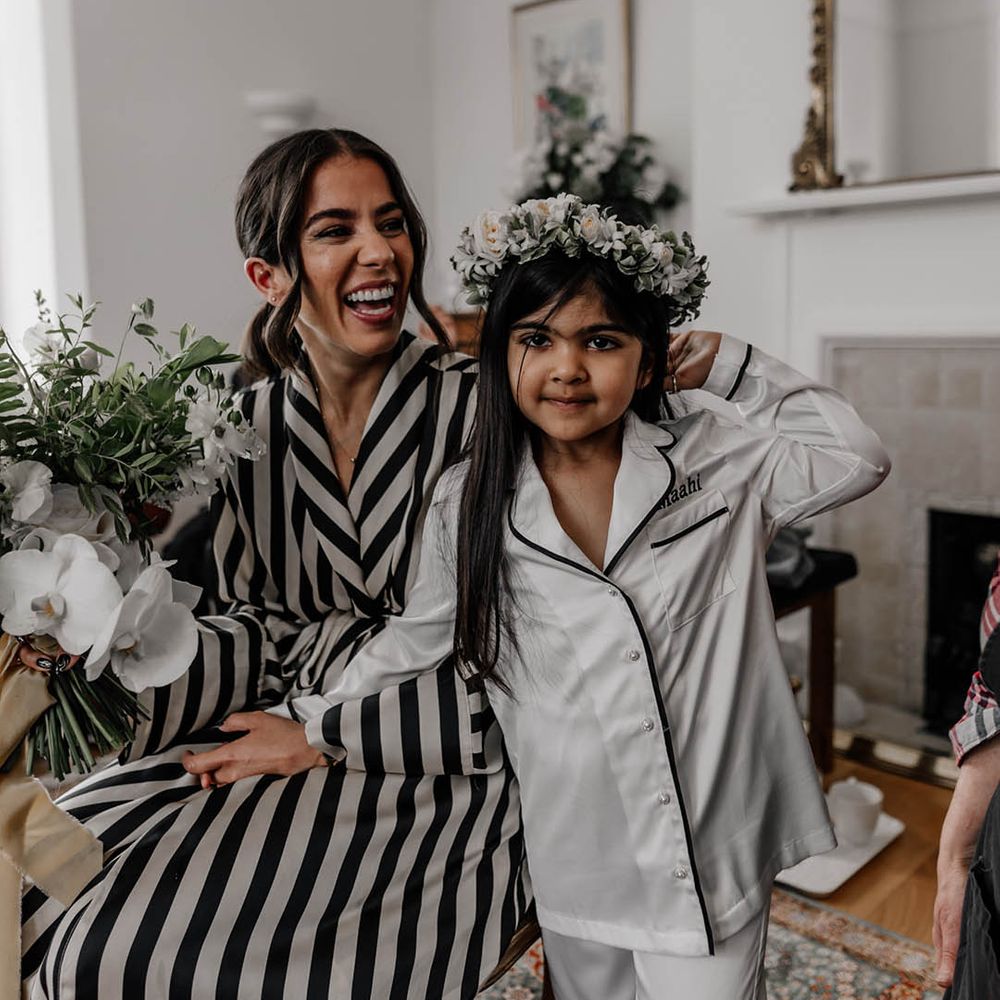 Bride in black and white stripy pyjamas on the wedding morning with the flower girl in white satin PJs and a flower crown 