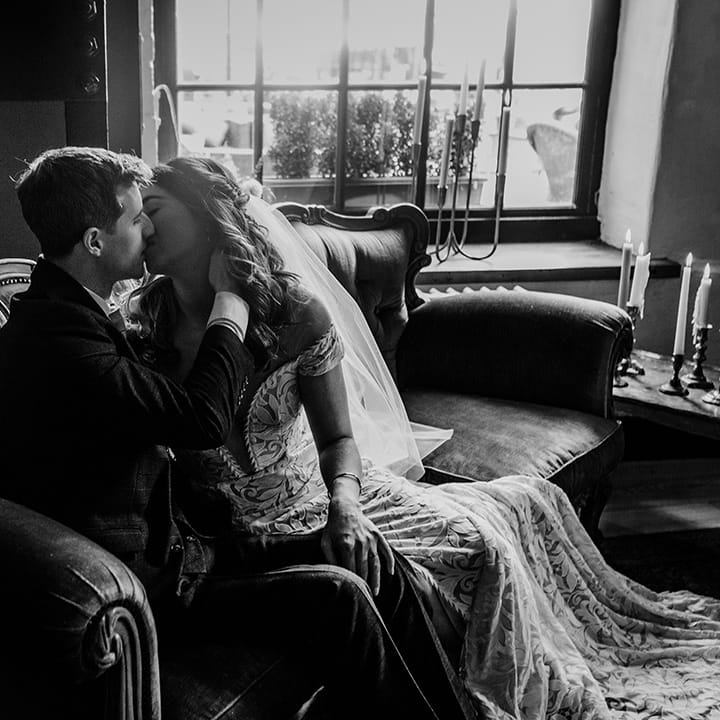 Bride and groom share an intimate kiss as they sit on a sofa together 