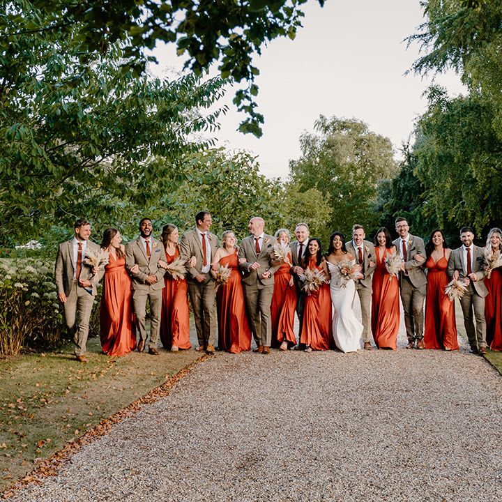 Wedding party shot of the bridesmaids in orange dresses and groomsmen in brown suits 