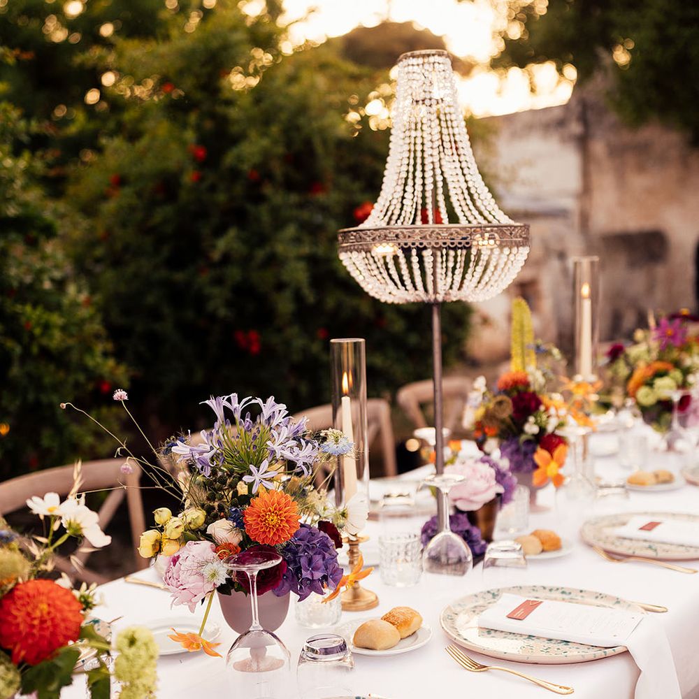 Outdoor destination wedding tablescape for Italian wedding with chandelier installations, colourful flower arrangements and speckled plates