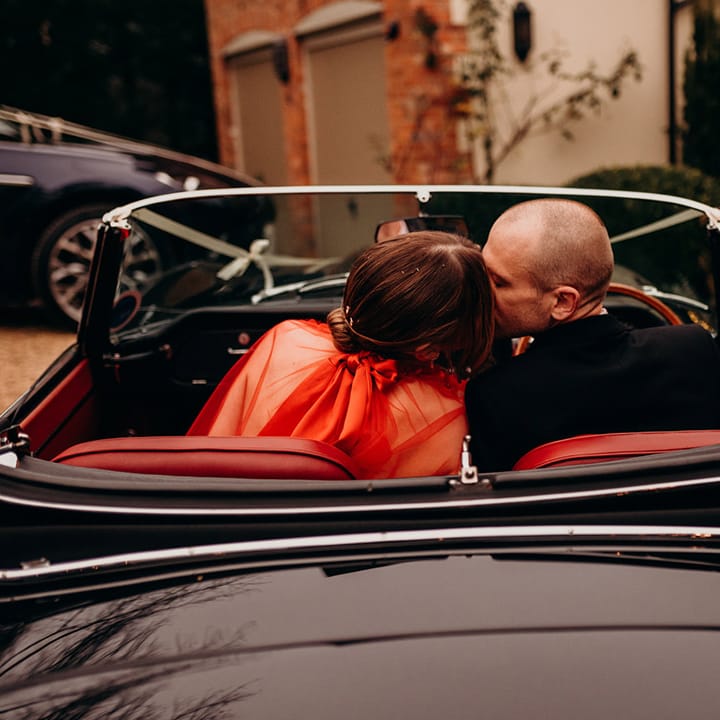 Bride and groom sitting in classic convertible wedding car at Christmas themed wedding
