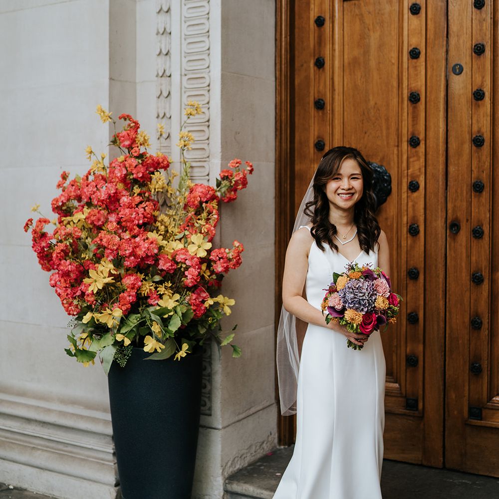 Bride wears her hair in loose curls whilst holding brightly coloured bridal bouquet 