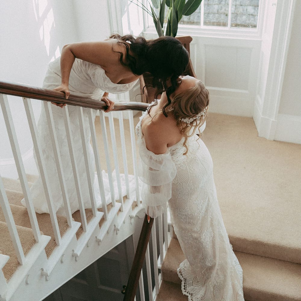 Brides in off the shoulder long sleeve wedding dress and strapless lace wedding dress kissing on the stairs