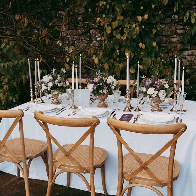 Intimate and neutral wedding tablescape with lavender and white tapered candles in gold candle holders, lavender wedding menus and mixed floral arrangements with white carnations, purple tulips, roses and foliage