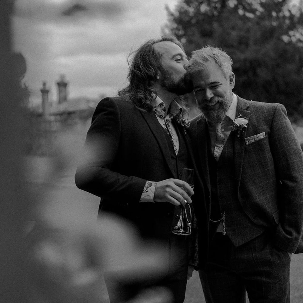 Grooms embrace in black & white image during couples portraits outdoors for botanical wedding