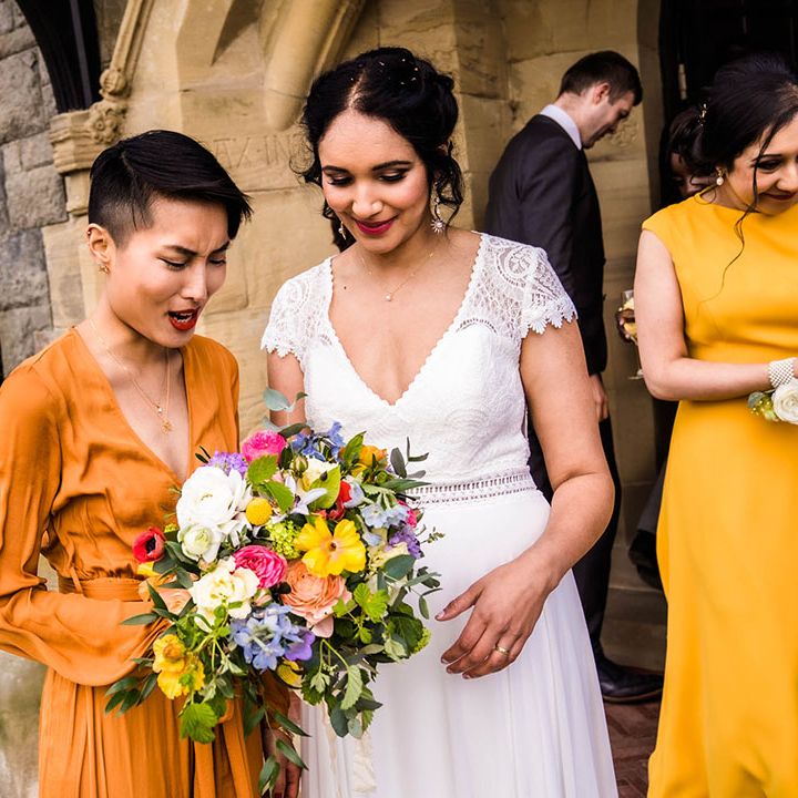 Bridesmaid wears orange wrap dress and holds colourful floral bouquet 