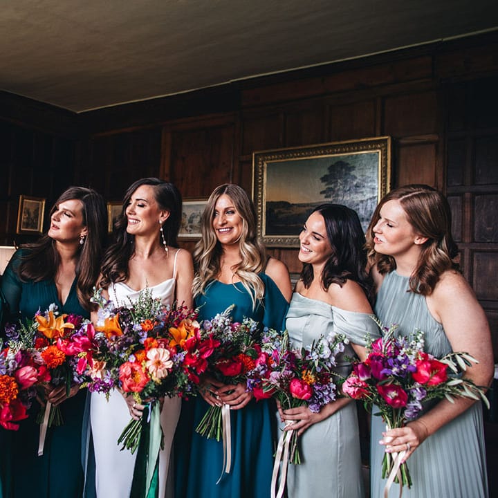 Bridesmaids in light and dark green mismatched bridesmaid dresses with the bride in a satin gown holding bright wedding bouquets 