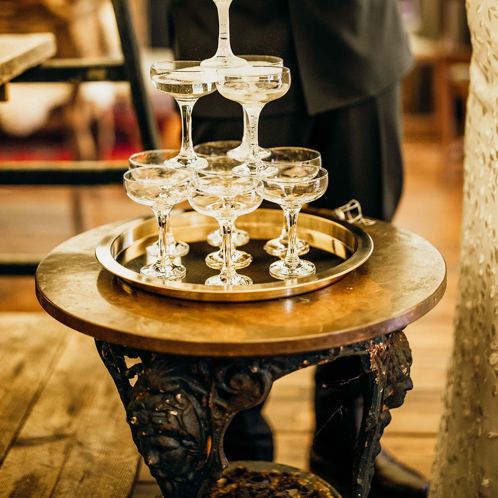 Bride & groom pour champagne into champagne tower during rustic wedding reception 