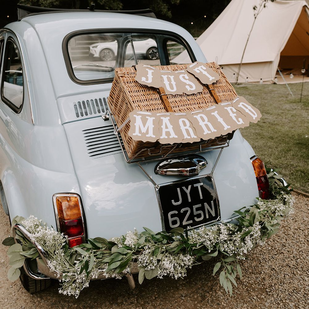 Light blue vintage Fiat 500 wedding car with wicker basket and 'Just Married' wedding sign attached to the back of the car