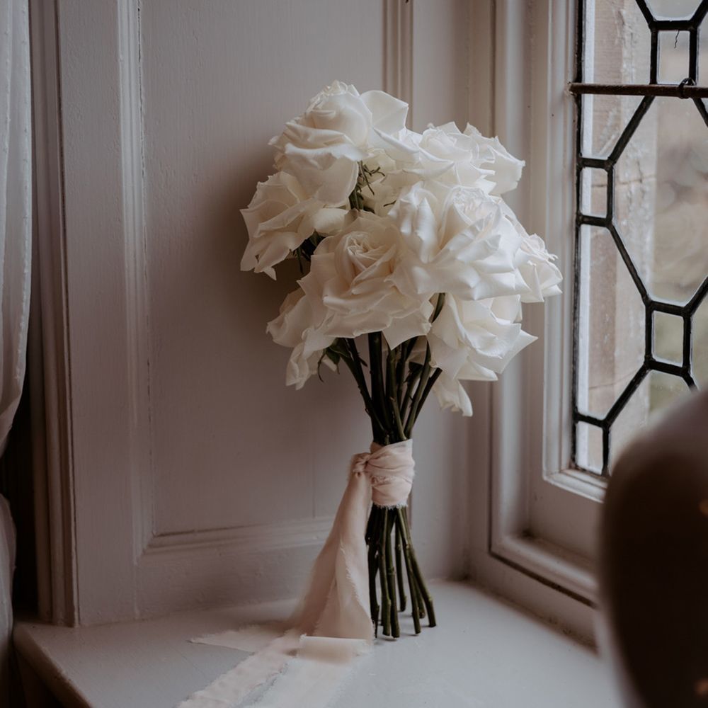 The bride's classic white rose wedding bouquet with long green stems tied with white ribbon 