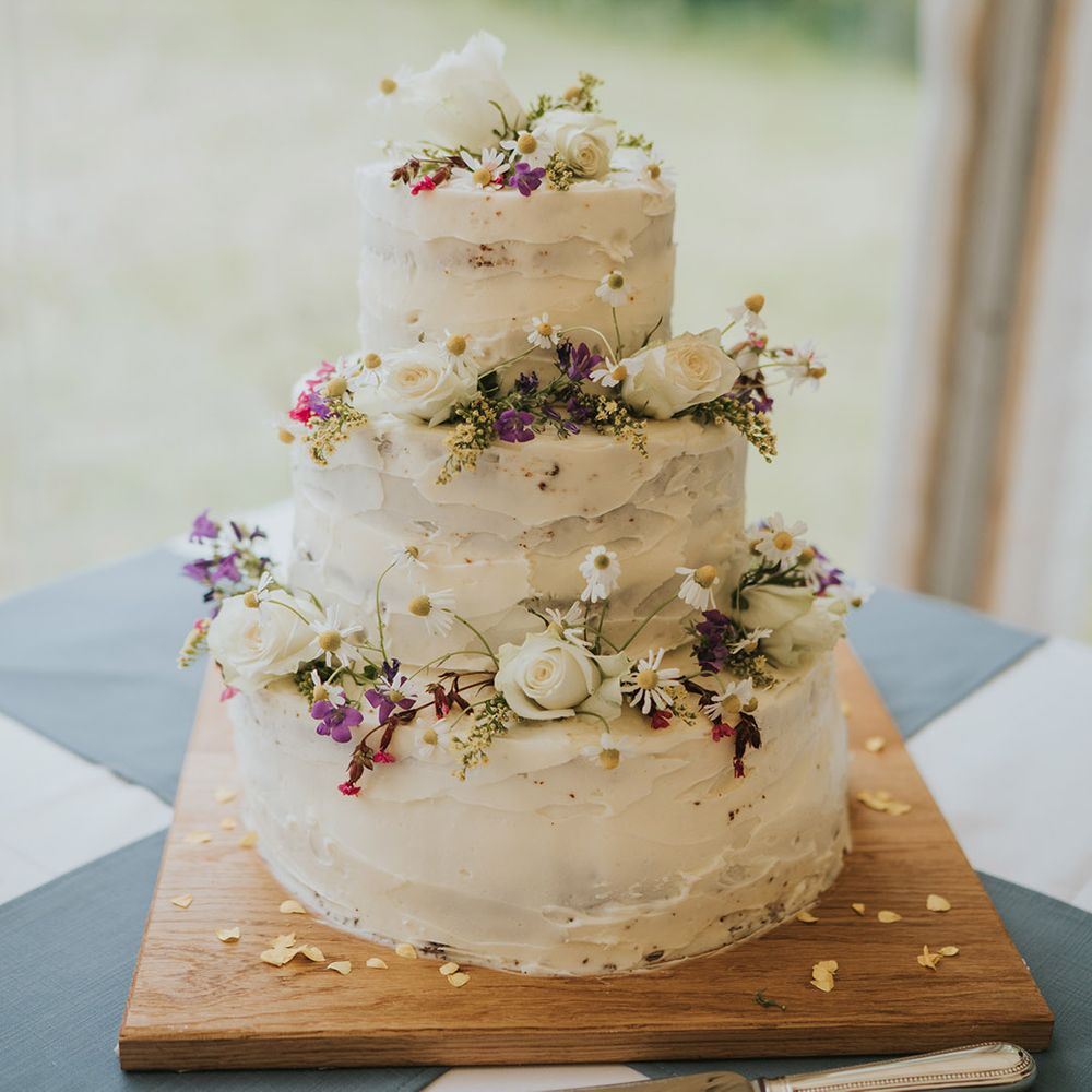 Three tier rustic white iced wedding cake with daisies and roses 