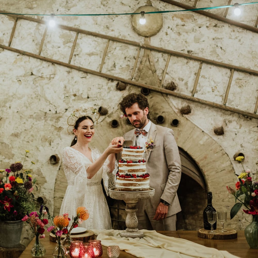 Bride and groom at rustic weddng venue in italy cutting a naked wedding cake covered in mixed berries