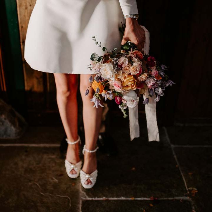 Bride in long sleeve short wedding dress and platform pearl wedding heels holding mixed bridal bouquet with garden roses, carnations, peonies and foliage 